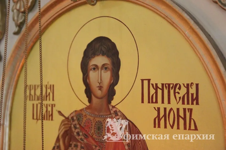 Крупный план иконы великомученика Пантелеимона в арочном киоте с надписью «Пантелеимонъ», перед иконой видна цепь лампады