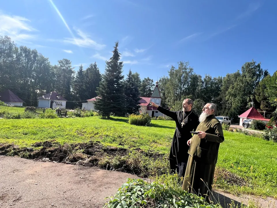 Клирик благословляет пустой травяной участок, вдали виден купол храма