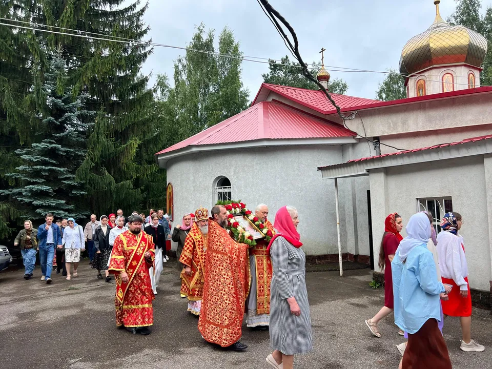 Крестный ход с духовенством и хоругвями обходит белый храм с красной кровлей и золотым куполом